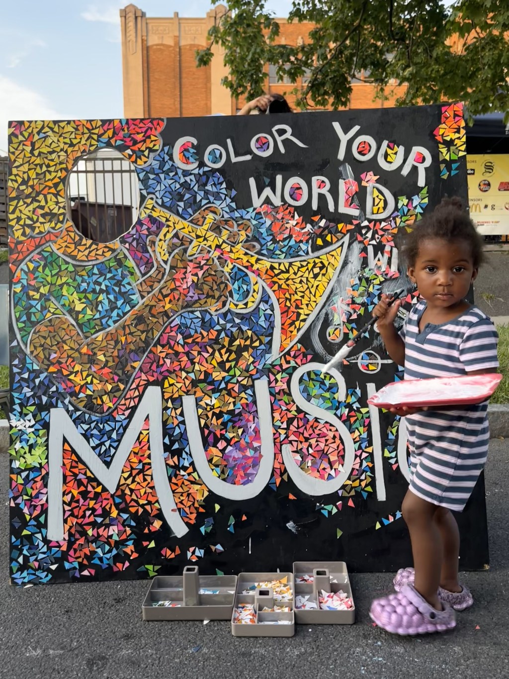 A young artist creating a paper mosaic using glue and paper on a wood board